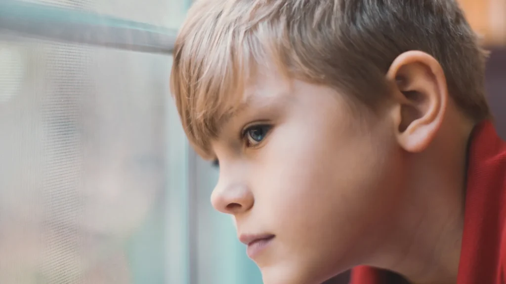 Young boy looking out a window symbol of father absence and resilience
