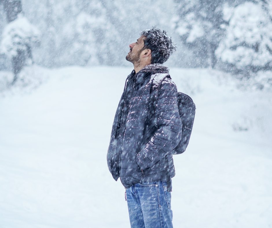 man in a winter jacket standing in falling snow, looking up toward the sky, illustrating vitamin D deficiency and its effect on mood, energy, and mental health in men